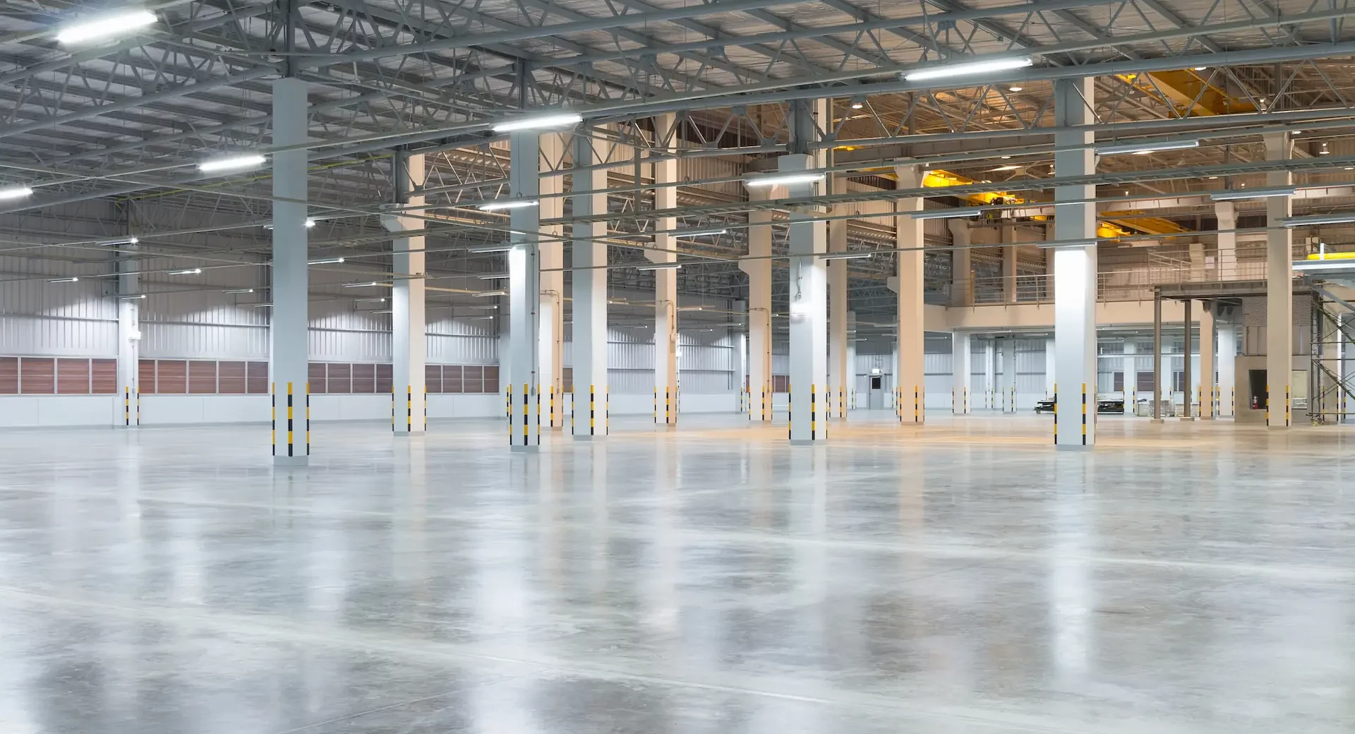 A large, industrial warehouse with concrete flooring sits open under fluorescent lighting.