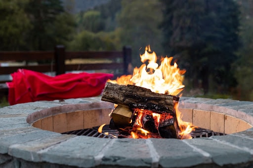 Close up of a fire in a round fire pit made of stone. Backyard summer safety tips include placing a fire pit over concrete and not putting flammable liquids in a fire pit