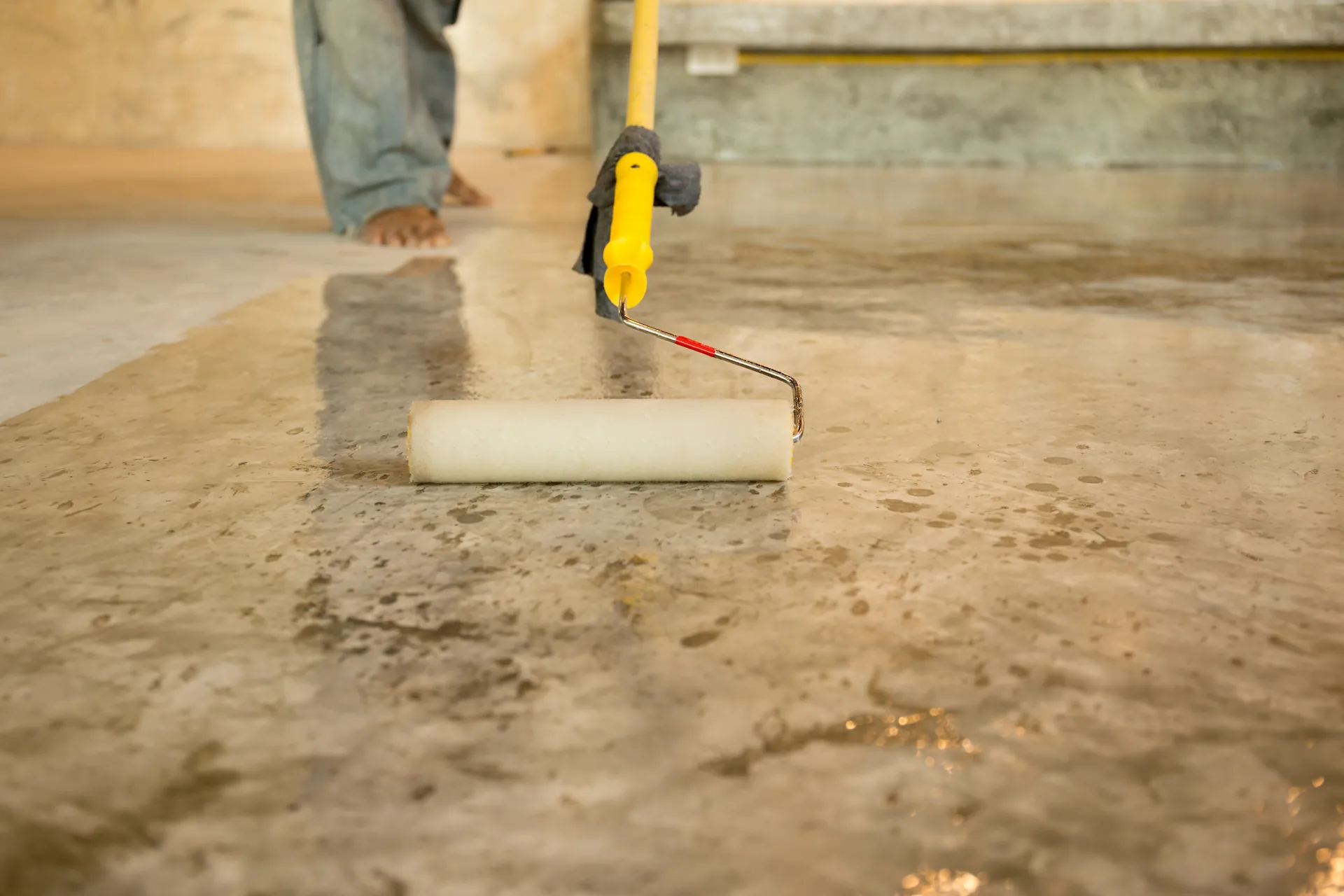 Closeup on an elegant concrete floor as a worker applies a sealing coat with a rolling foam brush. Sealing is one method through which you can improve the appearance of concrete floors.