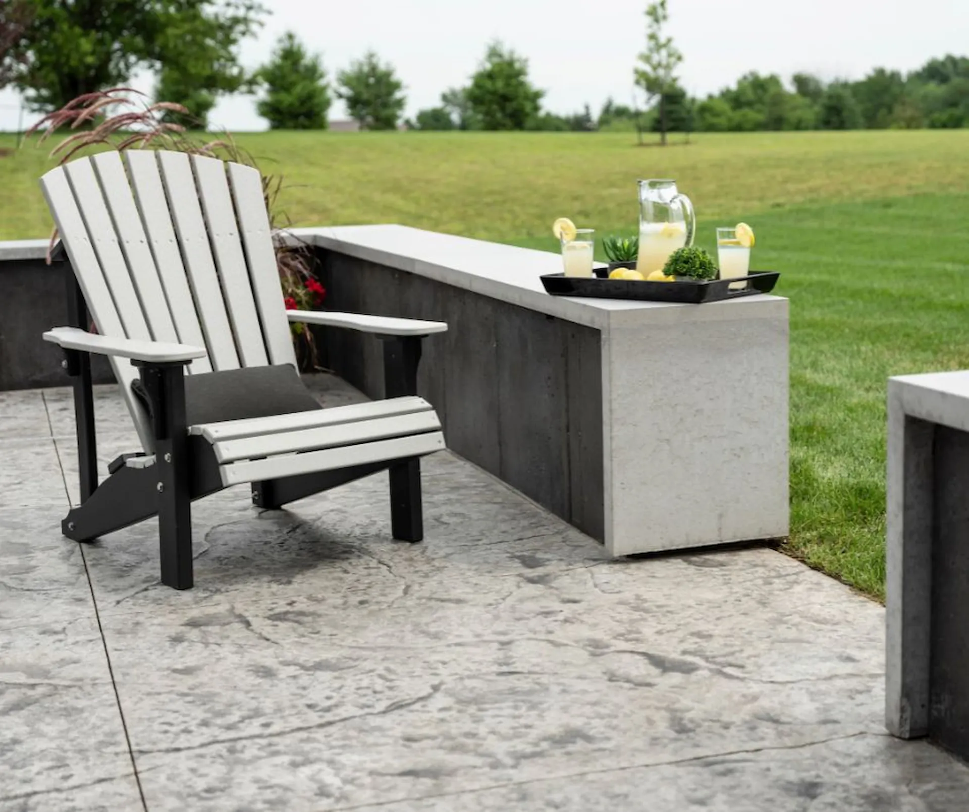 Medium shot of a grey, wooden lawn chair set on a stamped concrete patio. A slate texture pattern is one of the most popular stamped concrete applications for patios.