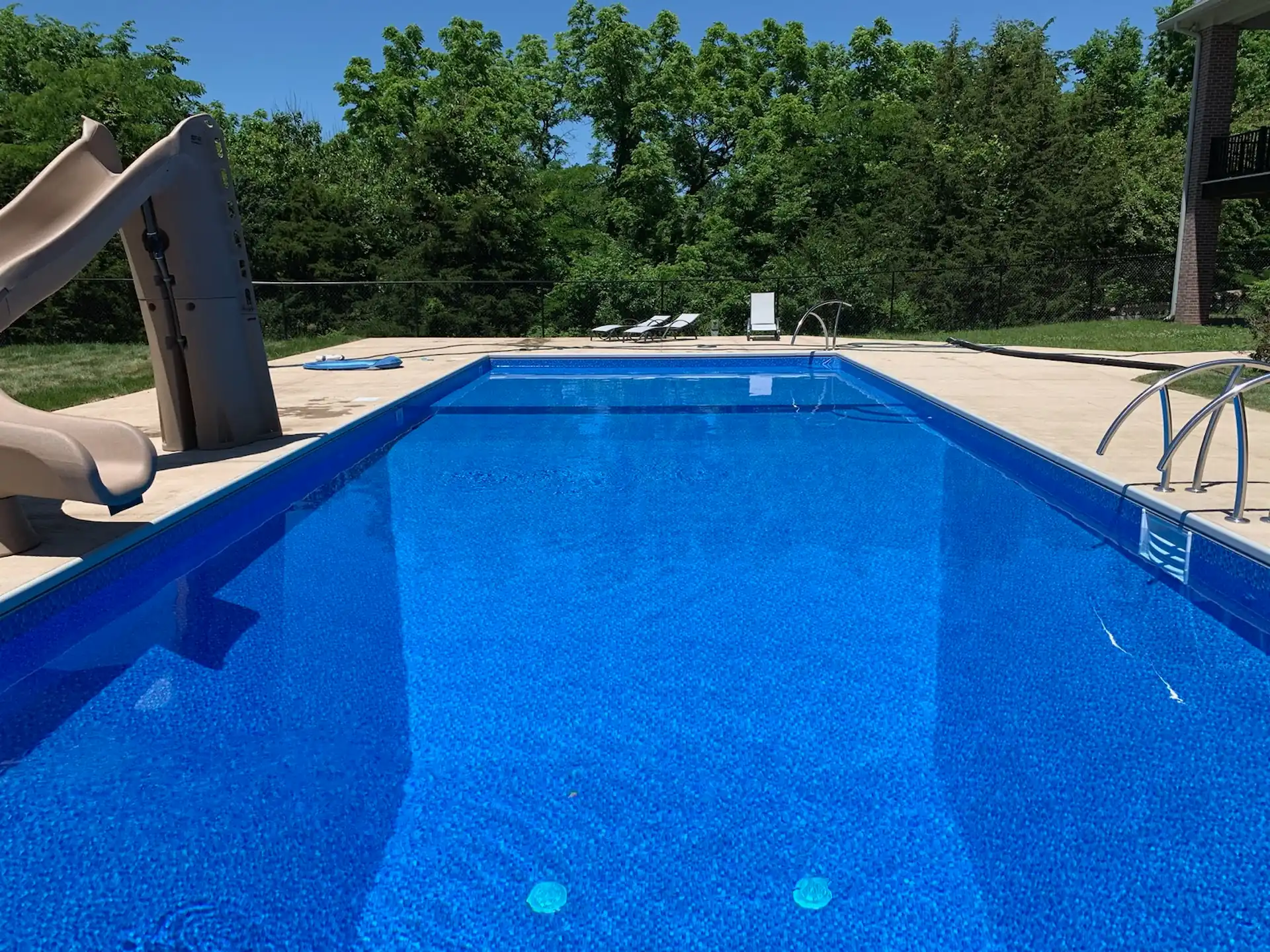 A rectangular inground pool with a blue liner sits in the sunlight. Pool maintenance is essential to preserving the look and functionality of pools like these.